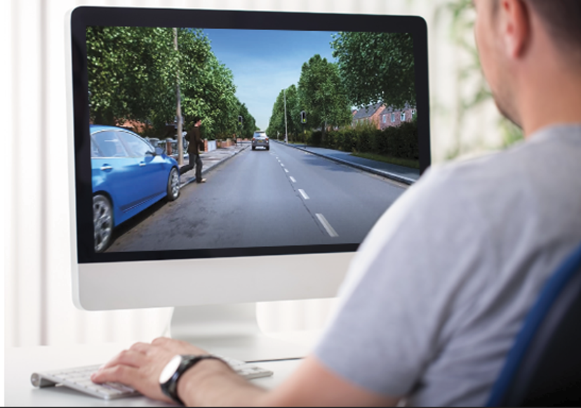 Driver completing an online hazard perception test on a desktop computer, watching a developing road scene with a pedestrian stepping into traffic.